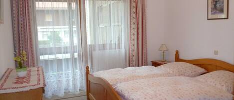Un dormitorio con una cama doble, una mesita de noche con lámpara, un aparador y una ventana con cortinas.
