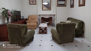 Una sala de estar con chimenea, dos sillones, un sofá, un televisor y un espejo decorativo.