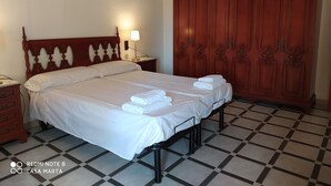 Una cama bien hecha con sábanas y toallas blancas, un cabecero de madera, una mesita de noche con lámpara y un armario grande.