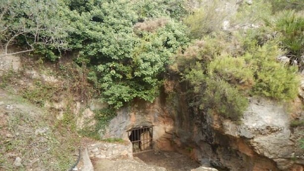 Una escalera de piedra que conduce a la entrada de una cueva, rodeada de vegetación.
