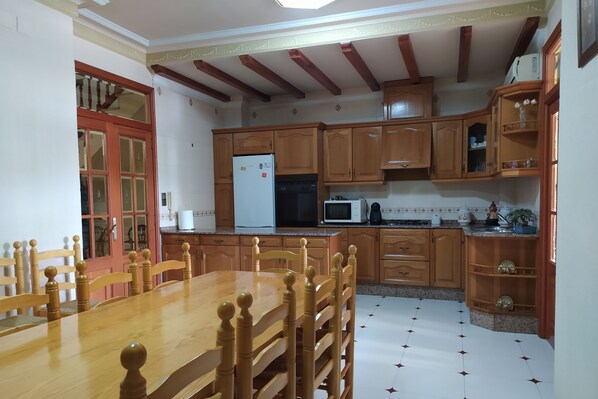 A kitchen with wooden cabinets, a dining table, and a refrigerator. - MarTa House - Chella (Chella)