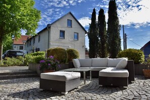 En terrasse med loungesæt, bord og krukker med planter.