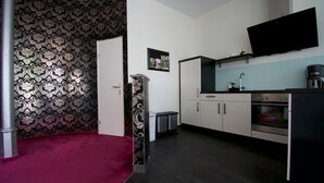 A compact kitchen with a microwave, oven, and sink. There is a door leading to another room and a small trash bin. - Apartment Faupel (Mülverstedt)