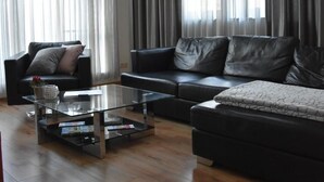 A modern living room with a black leather sofa, a glass coffee table, and a chandelier. - Apartment Faupel (Mülverstedt)