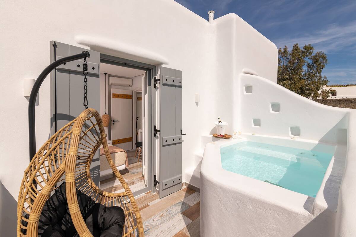Een witte villa met een privézwembad, een rieten stoel en een deur naar een badkamer.