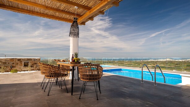 An outdoor seating area with wicker chairs and a table, overlooking a swimming pool and distant landscape.