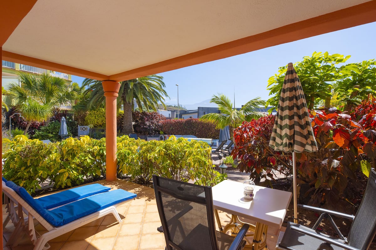 Ein überdachter Patio-Bereich mit Lounge-Möbeln, einem Tisch und einem Sonnenschirm.