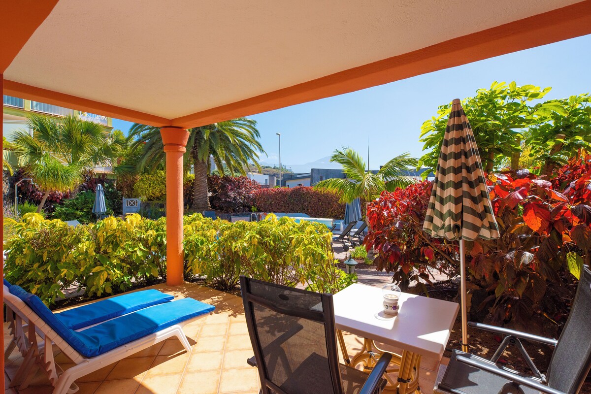 A covered patio area with lounge chairs, a table, and umbrellas.