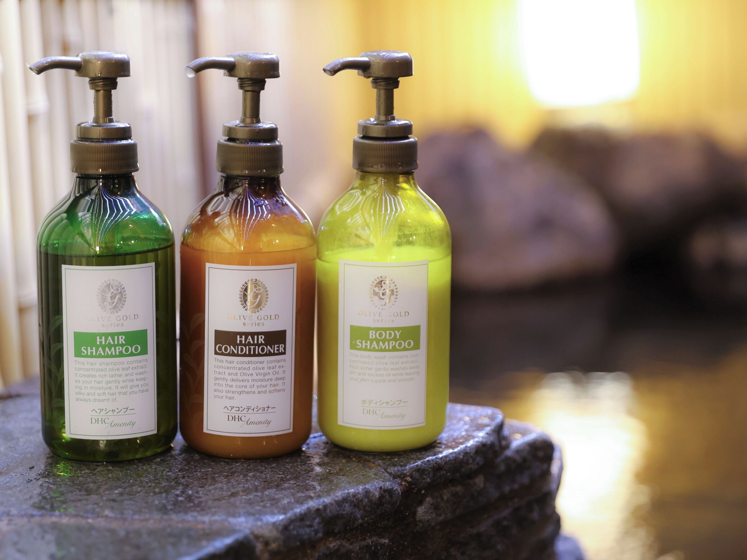 Tres botellas de productos para el cuidado del cabello sobre un repisa de piedra.