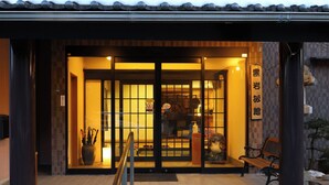 Edificio japonés tradicional con entrada de tejas, un letrero de madera y un banco afuera.