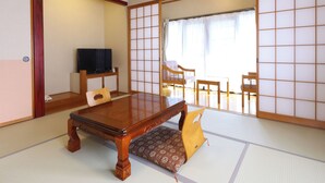 Una habitación tradicional japonesa con suelo de tatami, una mesa de madera baja, un televisor y puertas correderas shoji.