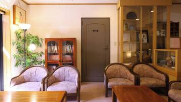 Una habitación con un armario de madera, dos sillones, una mesa de madera y una lámpara.