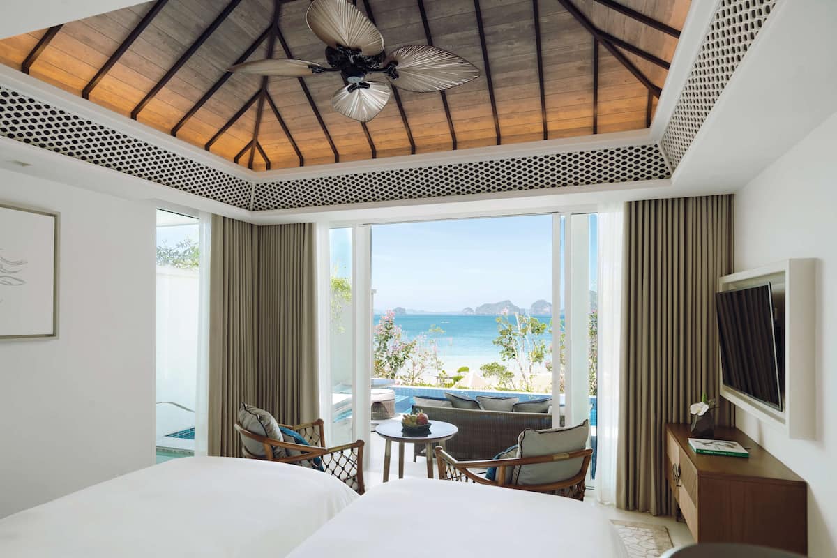 A hotel room with a bed, a seating area with chairs and a table, a television, and a view of the beach and ocean.