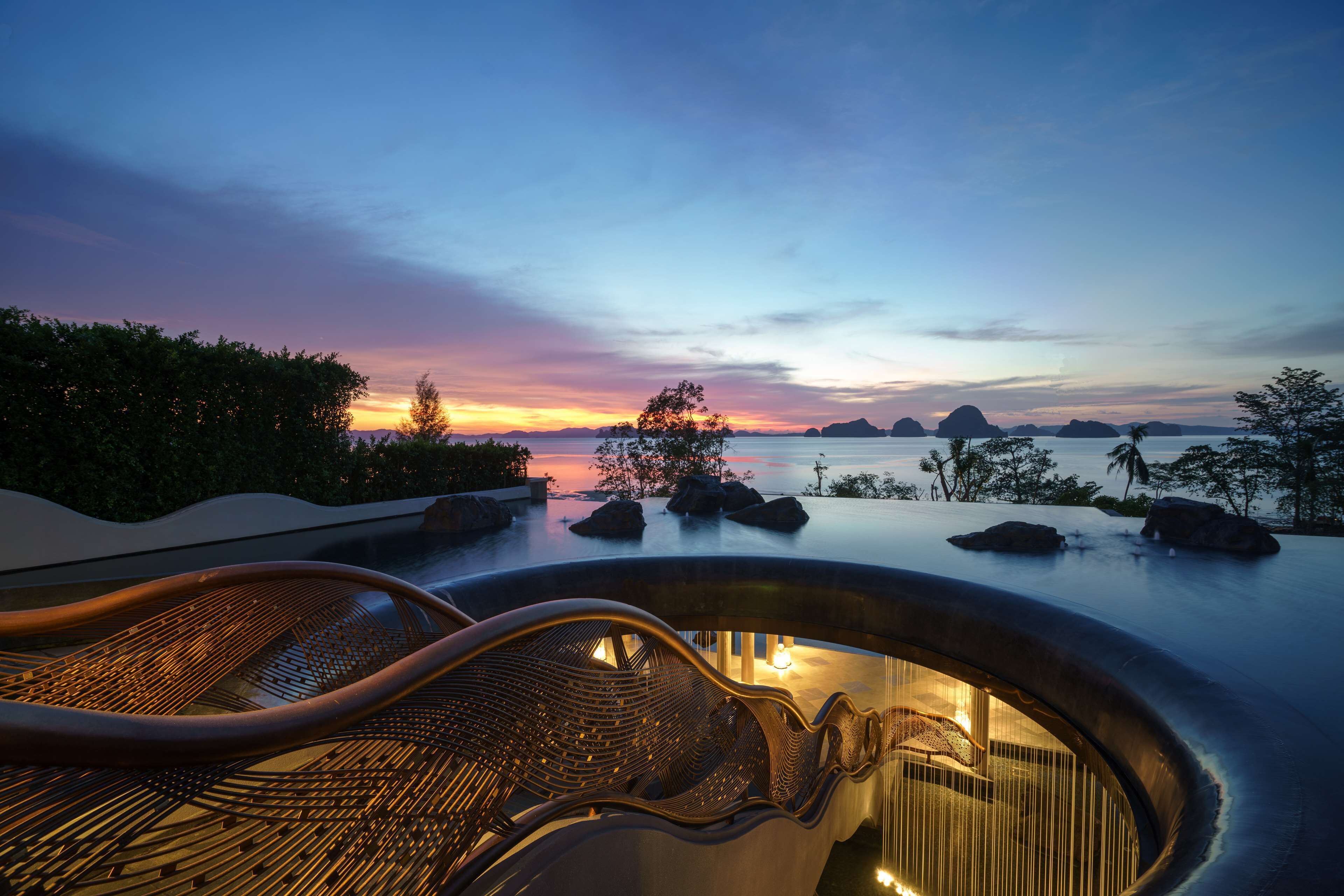 Een jacuzzi met uitzicht op de ondergaande zon boven water en eilanden.