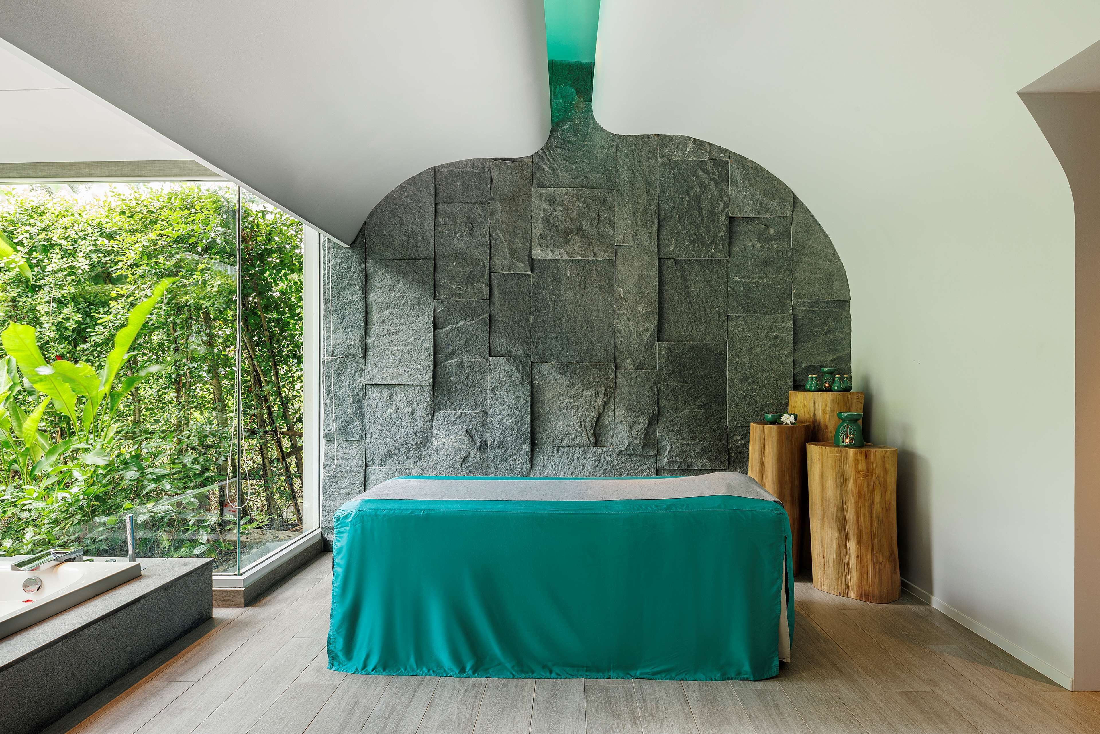 Un dormitorio moderno con una pared de piedra, una colcha color turquesa y una mesita de noche de madera.