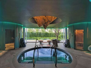 A spa area with a central pool, seating around the pool, and a view of greenery outside.