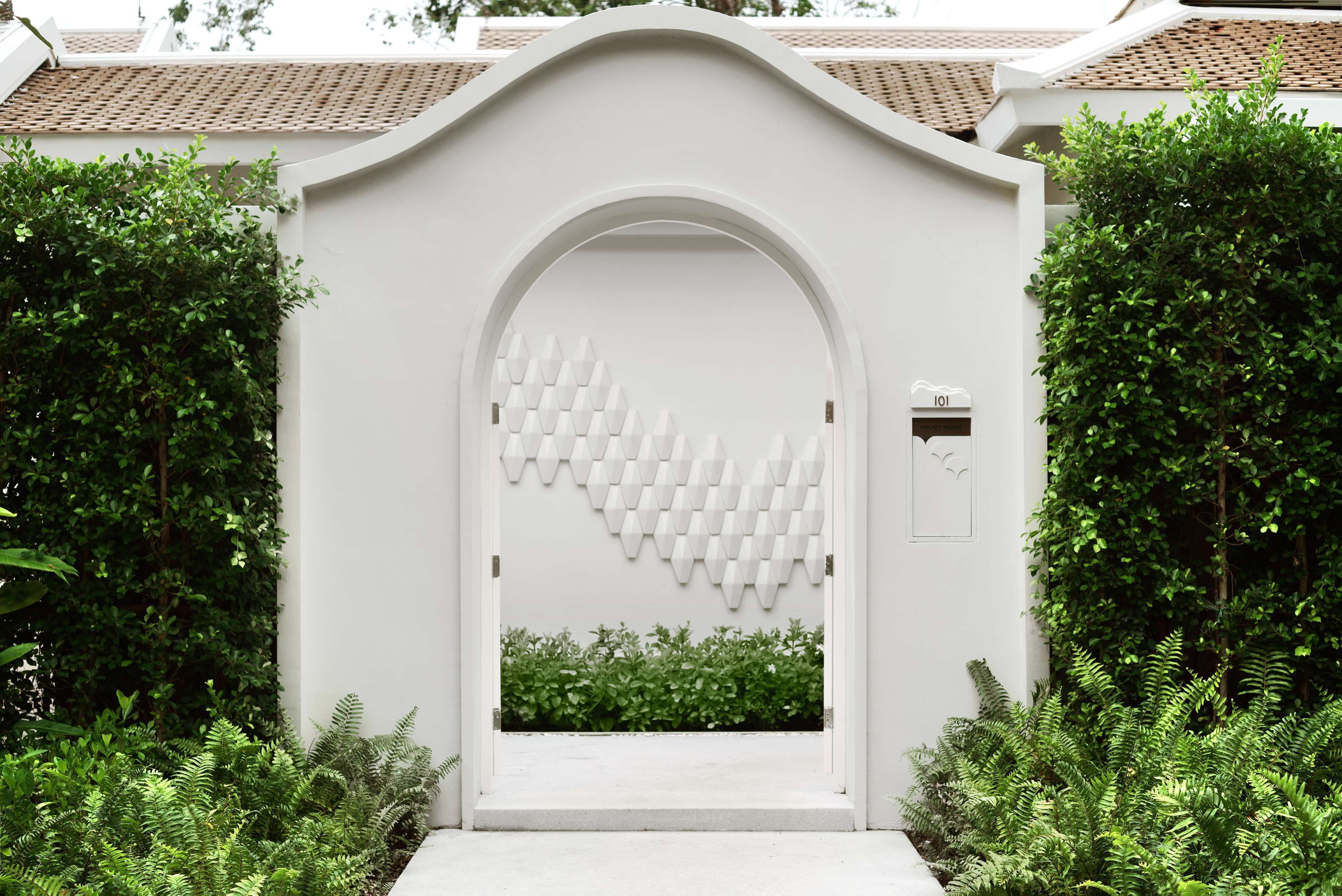 Un ingresso ad arco bianco con un motivo geometrico sulla parete, circondato da vegetazione lussureggiante.