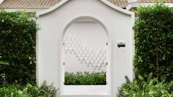 Un ingresso ad arco bianco con un motivo geometrico sulla parete, circondato da vegetazione lussureggiante.