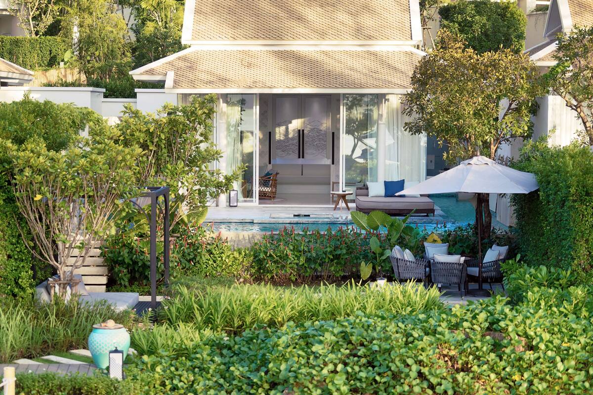 A modern house with a pool, surrounded by lush greenery and a patio area with outdoor furniture.