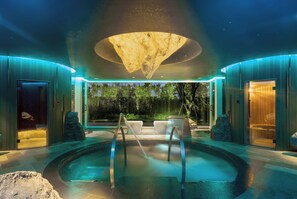 A modern spa with a heated pool, stone seating, and a large, illuminated ceiling feature.