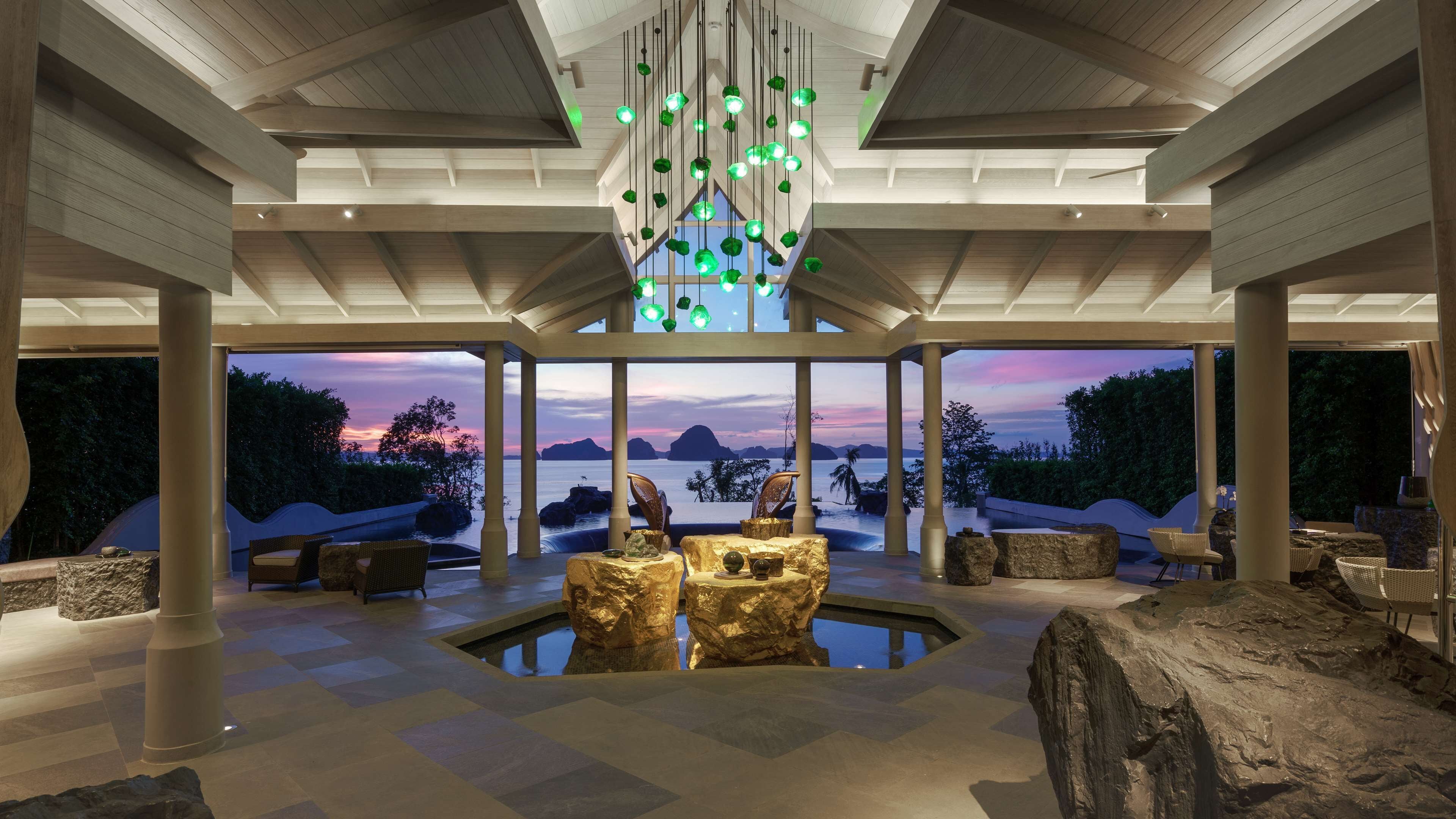 A modern interior with a central pool, seating areas, and a view of the sunset over water.