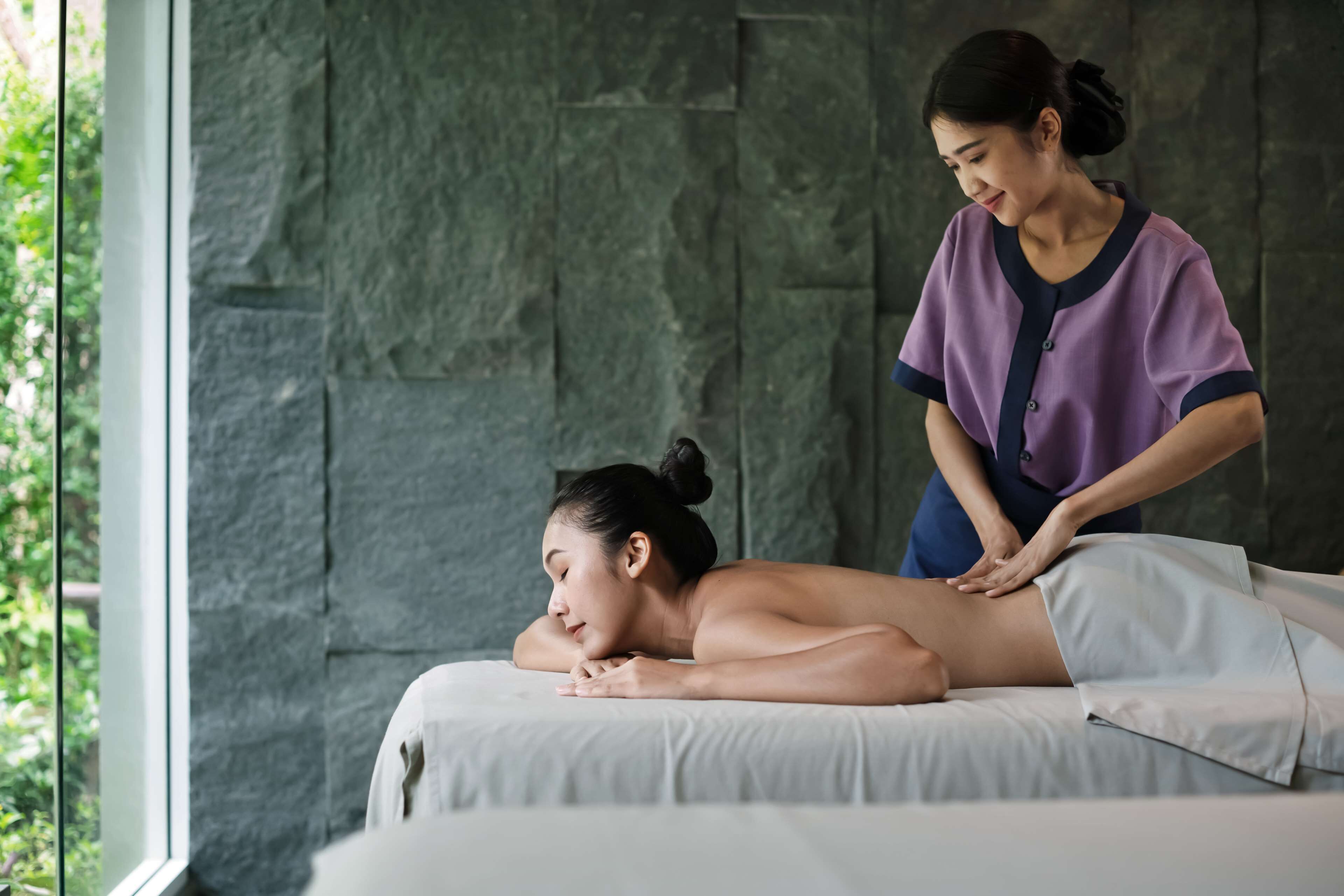 A massage therapy session in a room with a stone wall and a large window.