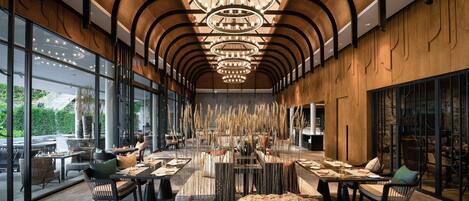 A spacious indoor area with multiple tables and chairs, large windows, and a distinctive ceiling design.