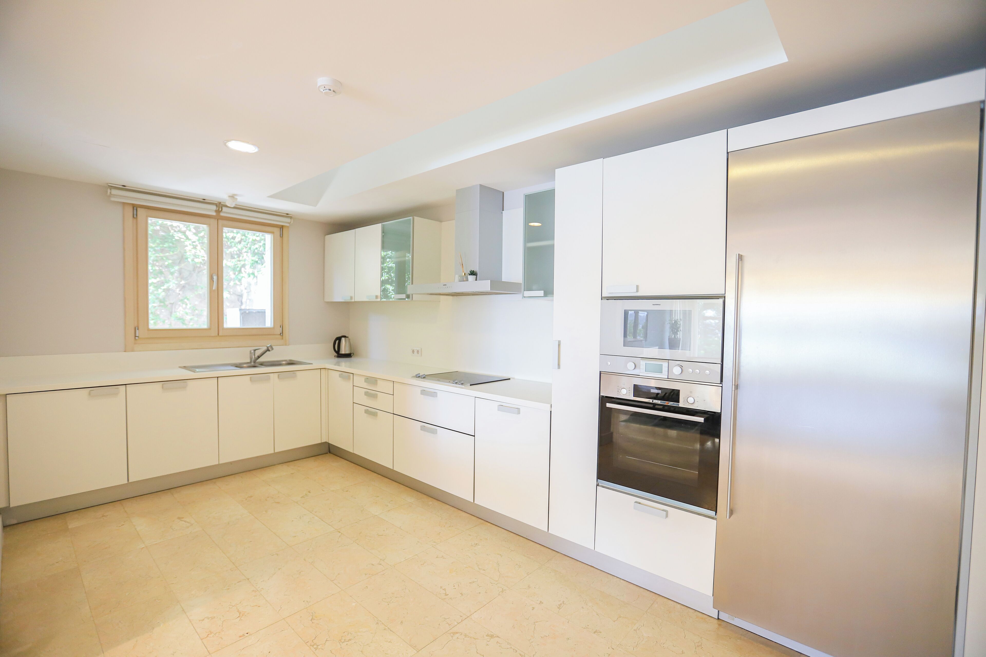 A modern kitchen with white cabinets, a stainless steel refrigerator, and a built-in oven.