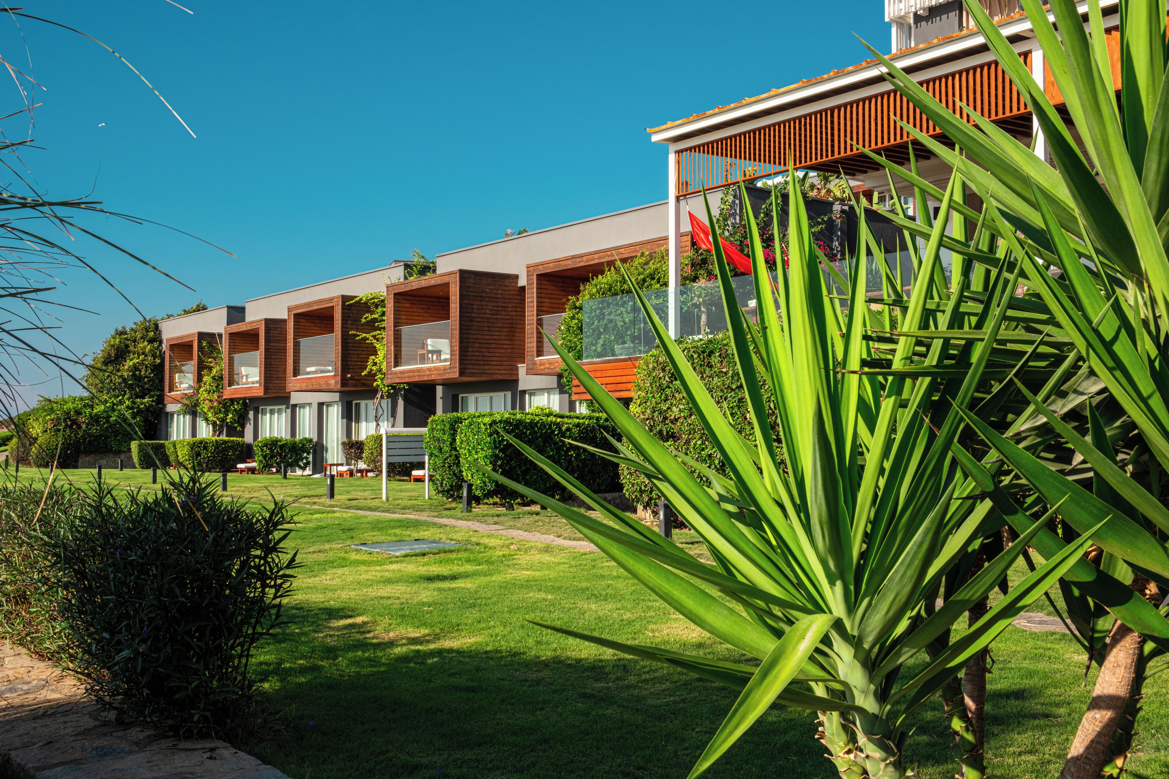 A modern building with multiple balconies, a well-maintained lawn, and surrounding greenery.