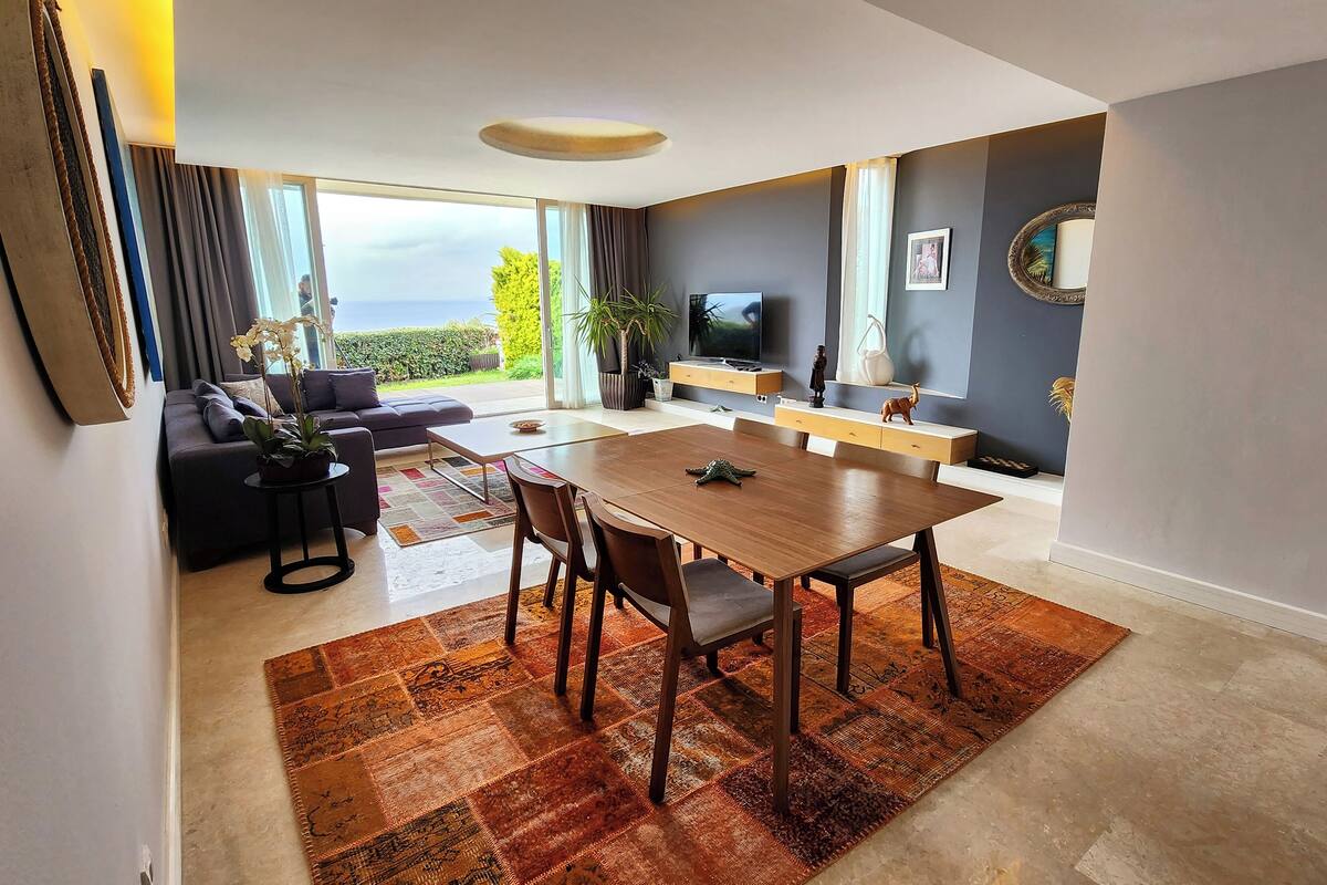 Una sala de estar moderna con comedor, un sofá, un televisor y un gran ventanal con vistas.