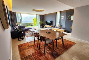A modern living room with a dining area, a sofa, a TV, and a large window with a view.