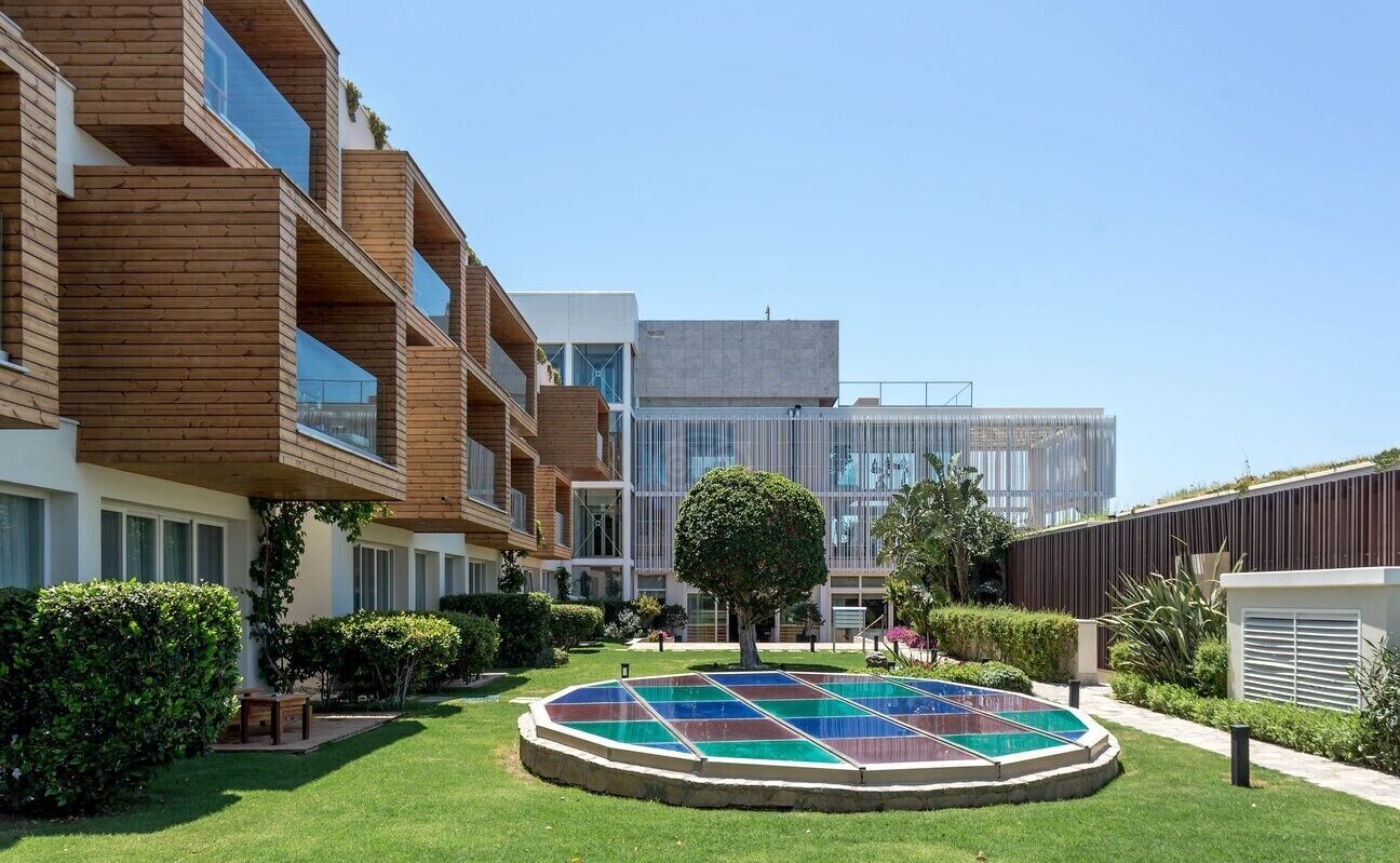 A modern building with wooden balconies, a central courtyard with a colorful mosaic, and a clear blue sky.