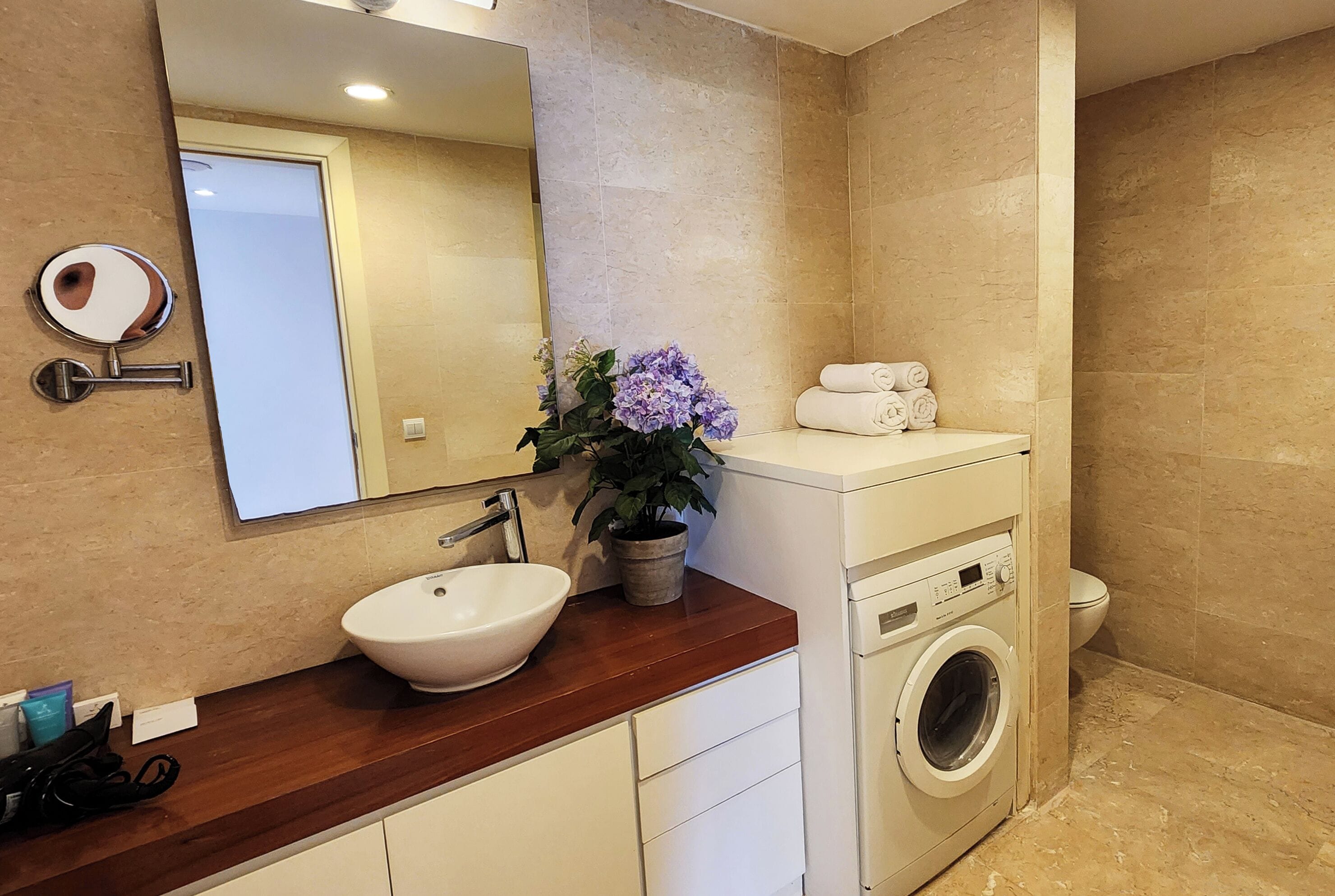 A bathroom with a sink, mirror, potted plant, towels, and a washing machine.