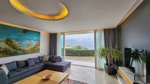 A modern living room with a sectional sofa, a coffee table, and a large painting of a tropical landscape. - Palmalife Bodrum Resort & Spa (Bodrum)