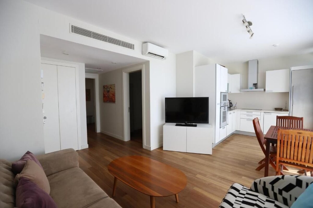 A modern living room with a sofa, a coffee table, a TV, and a dining area with a table and chairs.