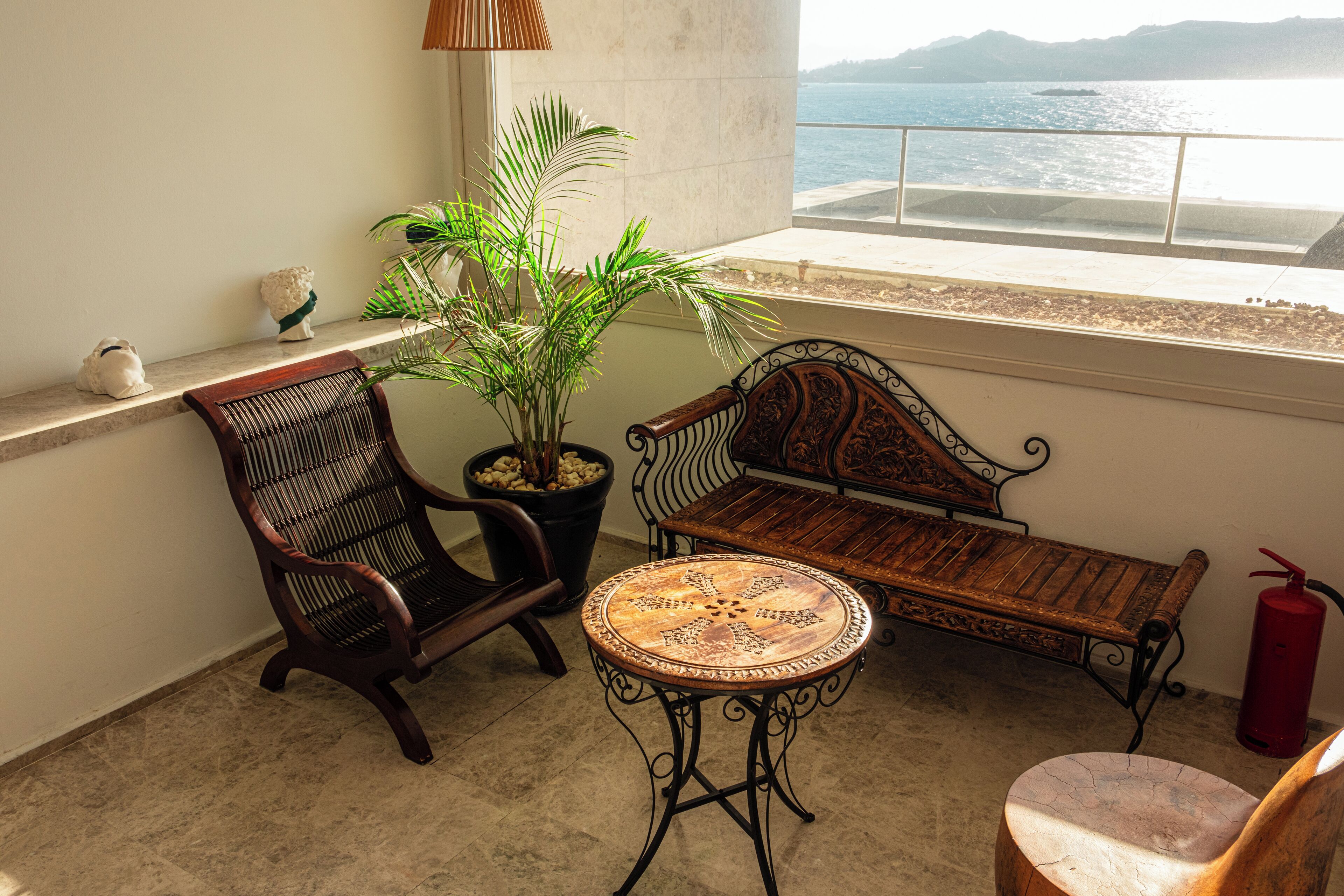 A balcony with a wooden bench, a chair, and a small table. There is a potted plant and a decorative item on the wall.