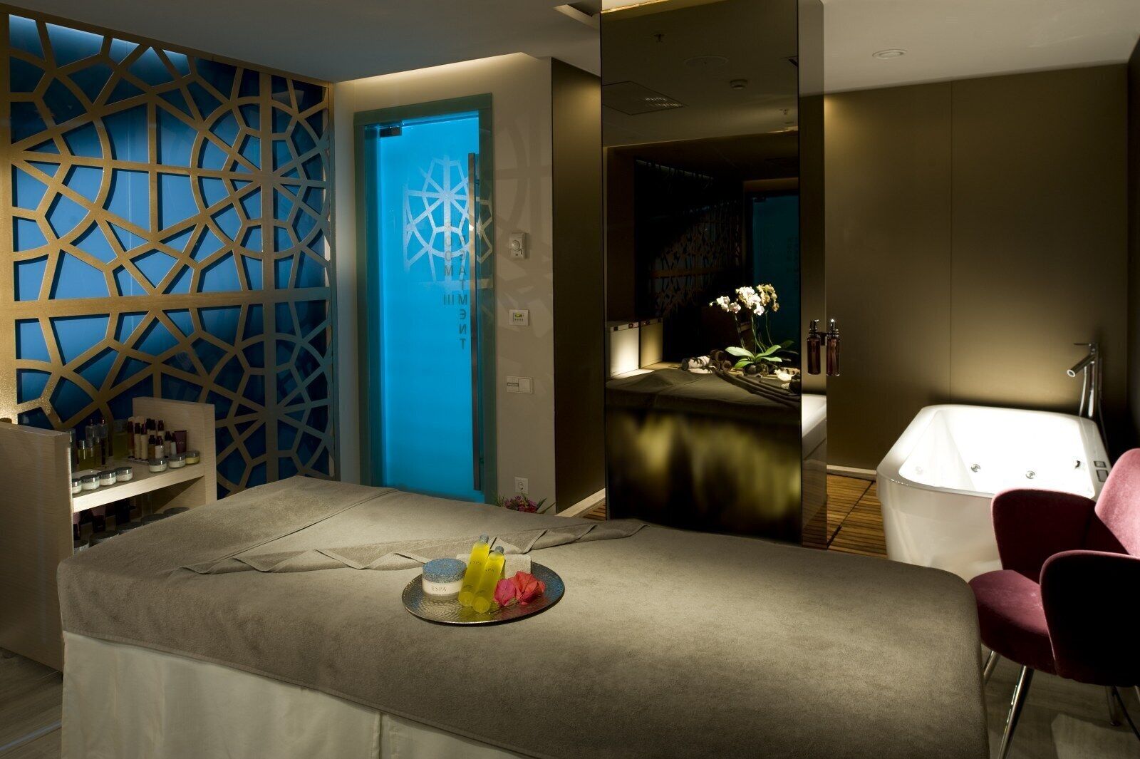 Une salle de spa moderne avec une table de massage, une porte bleue et une baignoire blanche.
