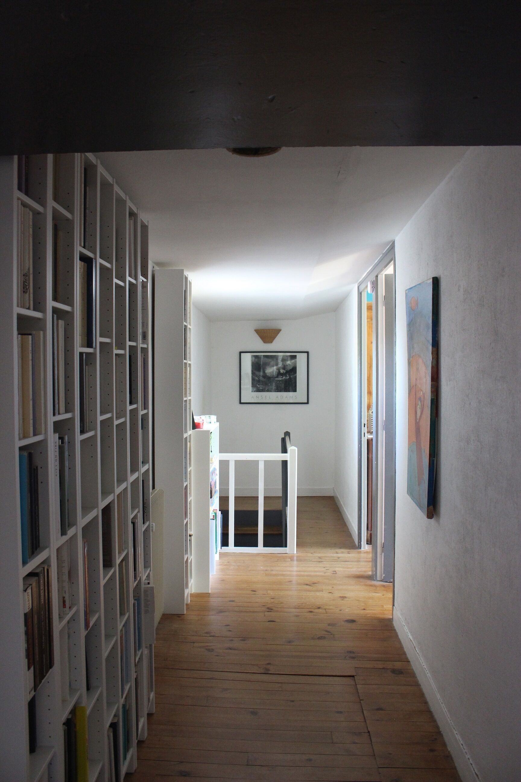 Un passadís estret amb terres de fusta, parets blanques i una banca blanca. A l'esquerra, prestatgeries plenes de llibres, i a la paret dreta, un quadre emmarcat.