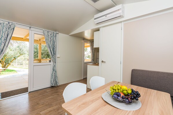 A modern kitchen with white cabinets, a dining table with a fruit bowl, and a sliding glass door leading to a garden.