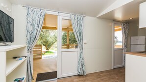 A modern kitchen with white cabinets, a wooden countertop, and a sliding glass door leading to a wooden deck. - Mobile Home Pecten 04 (Pakostane)