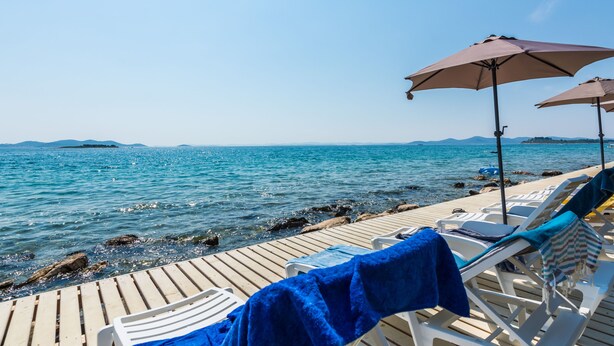 A wooden deck with lounge chairs and umbrellas overlooking a calm sea. - Mobile Home Pecten 04 (Pakostane)