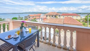 A balcony with a table set for breakfast, overlooking a coastal town with red-roofed buildings and a clear sky. - Apartments Anchor (Pasman)