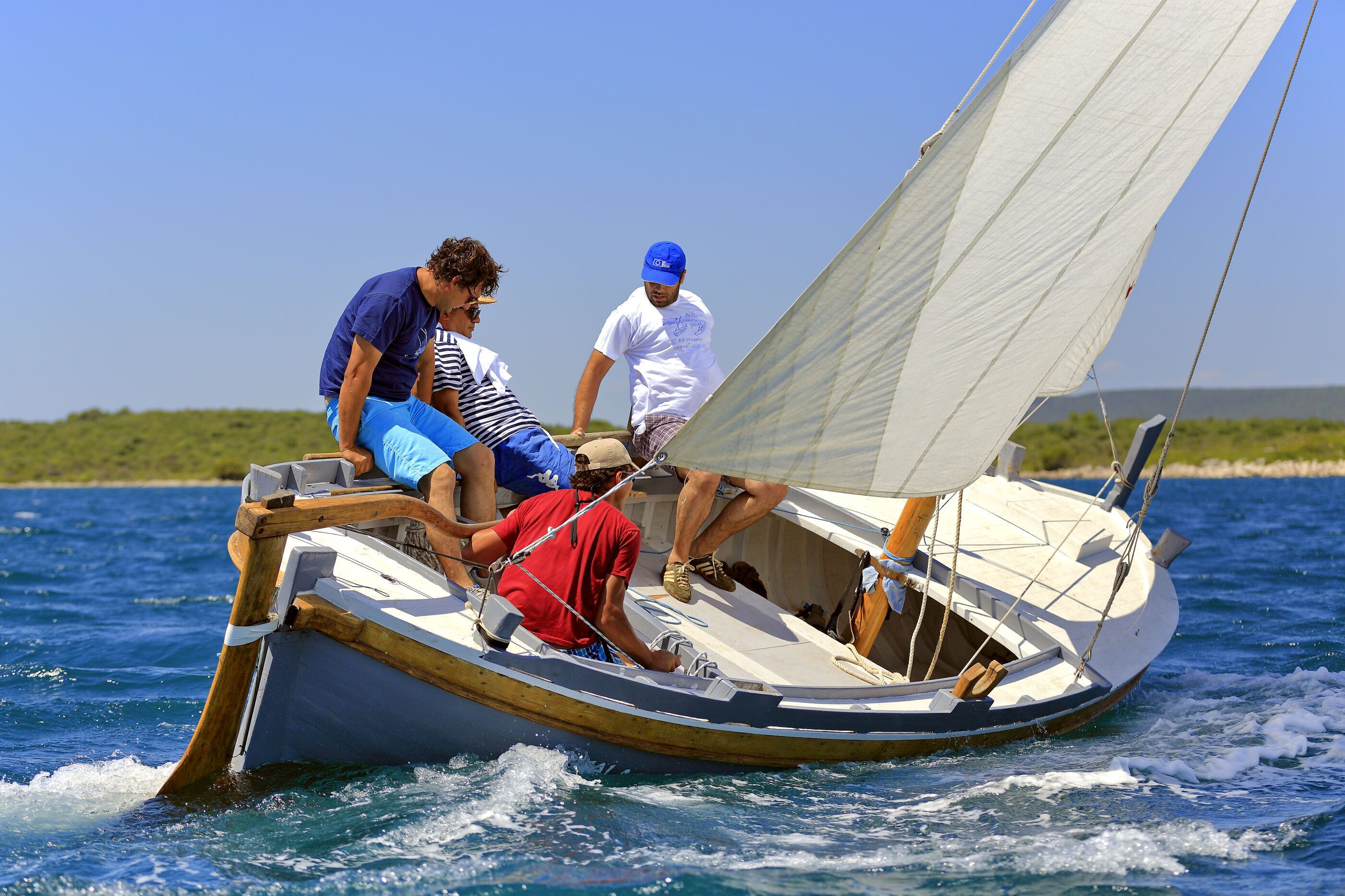 A small sailboat with three people on board, one steering and two passengers.