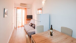 A room with a bed, a TV, a refrigerator, and a dining table with wine glasses. - Apartments Anchor (Pasman)
