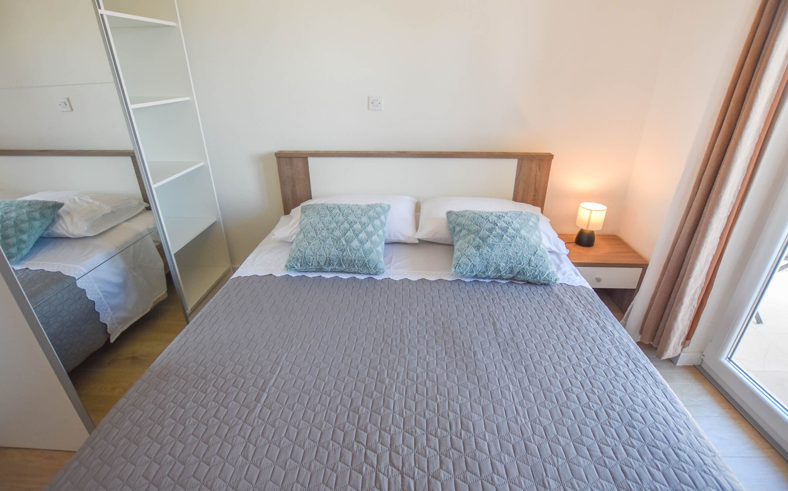 A neatly made bed with a grey quilt, two pillows, and a bedside lamp.