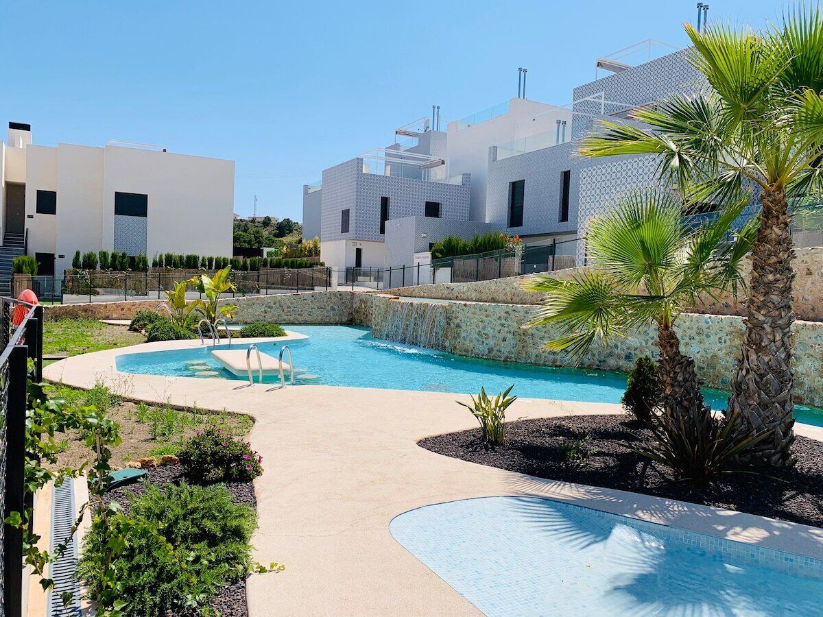 A modern pool area with a clear blue pool, surrounded by palm trees and a stone wall.