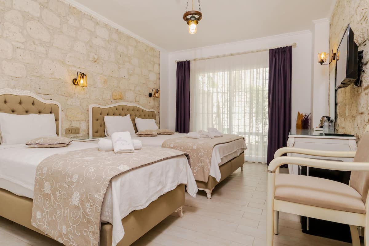 A hotel room with two beds, a desk, a chair, and stone walls.