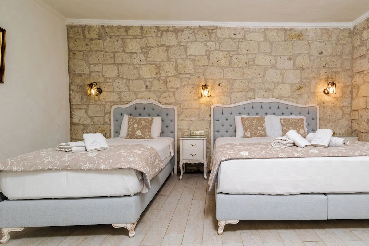 A double room with two beds, each with a nightstand, against a stone wall.