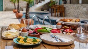 A breakfast table with various foods and drinks, including eggs, bread, and fruits, near a pool area. - Avlu Alacati Butik Otel (Cesme)