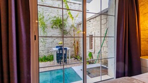 A room with a sliding glass door leading to a courtyard with a small pool, a table with chairs, and potted plants. - Avlu Alacati Butik Otel (Cesme)